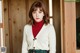 A woman in a white cardigan and a red turtle neck sweater.