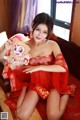 A woman in a red dress sitting on a bed holding a monkey.