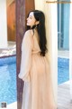 a woman standing in front of a pool wearing a beige dress