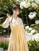 A woman in a yellow and white dress standing in front of flowers.