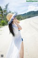 A woman in a white dress and a straw hat on a beach.