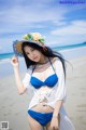 A woman in a blue bikini and a straw hat on the beach.