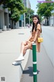 A woman sitting on a green pole on the side of a street.