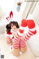 A woman in a red and white striped outfit is sitting on a bed.