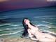 A naked woman laying in the ocean on a beach.