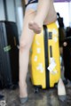 A woman sitting on top of a yellow suitcase.