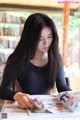 A woman sitting at a table reading a magazine.