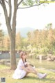 A woman in a white dress sitting under a tree.